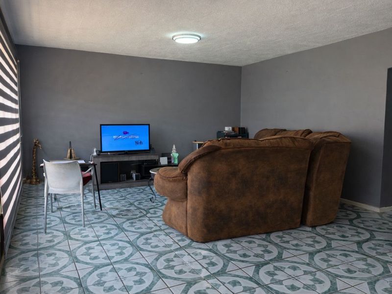 A living room featuring patterned ceramic floor tiles, grey painted walls, and roller blinds, providing a functional and neutral living space.