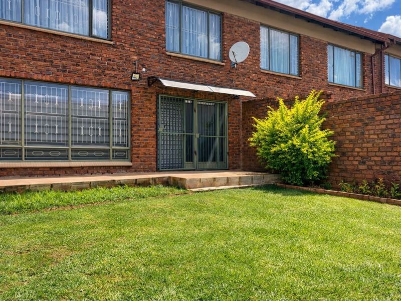 Rear view of the apartment featuring a face brick facade, a private garden, and a concrete patio area with security features.