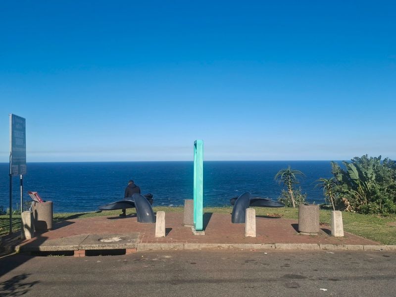 A scenic coastal lookout point featuring a paved area, concrete bollards, and expansive ocean views.