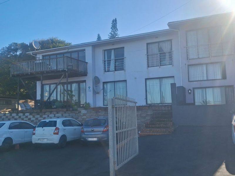 Front elevation of a multi-level residential property featuring a raised wooden deck, sliding glass doors, and a paved driveway with security gate.