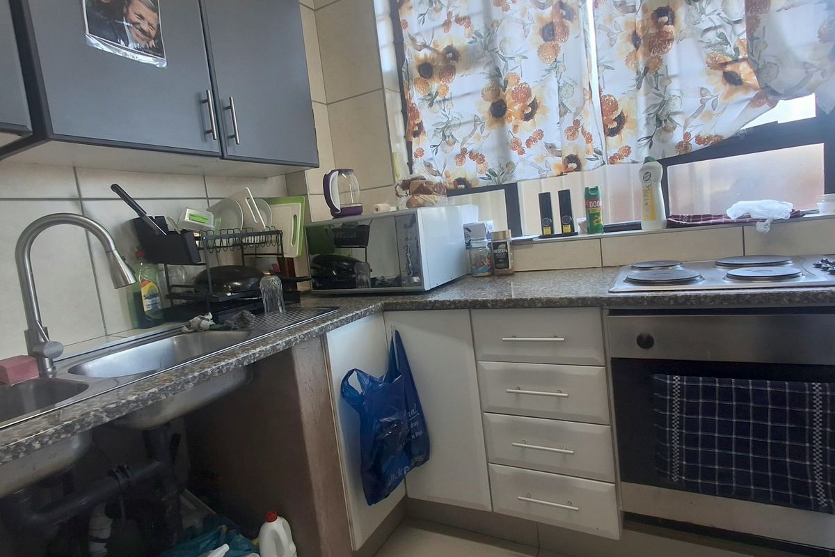 A functional kitchen featuring built-in cabinetry, a stainless steel sink, and integrated oven and hob, with tiled backsplash and laminate countertops.