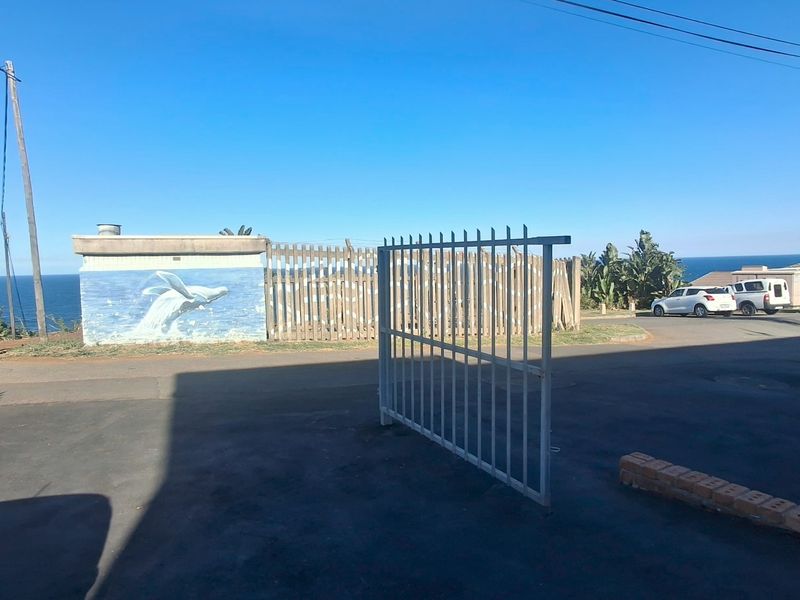 Street-level view of the property entrance featuring a metal security gate, asphalt driveway, and a perimeter wall with a decorative mural overlooking the ocean.