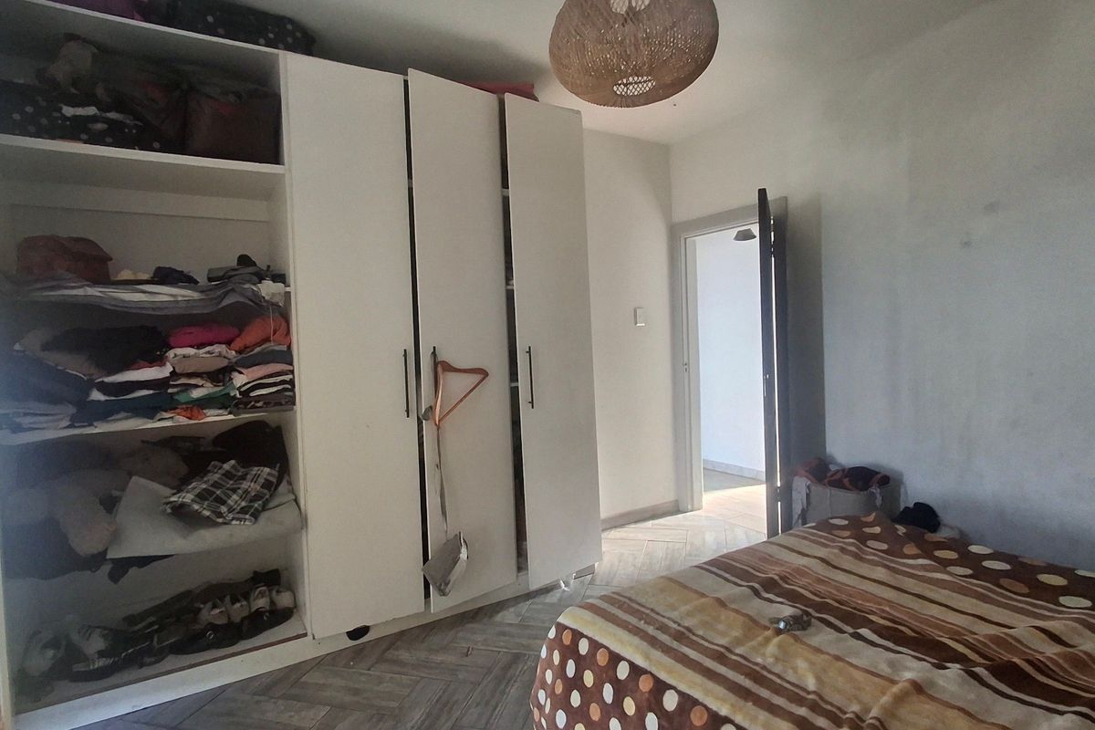 A bedroom featuring built-in wardrobes and herringbone tile flooring, requiring minor cosmetic updates to the wall finishes.