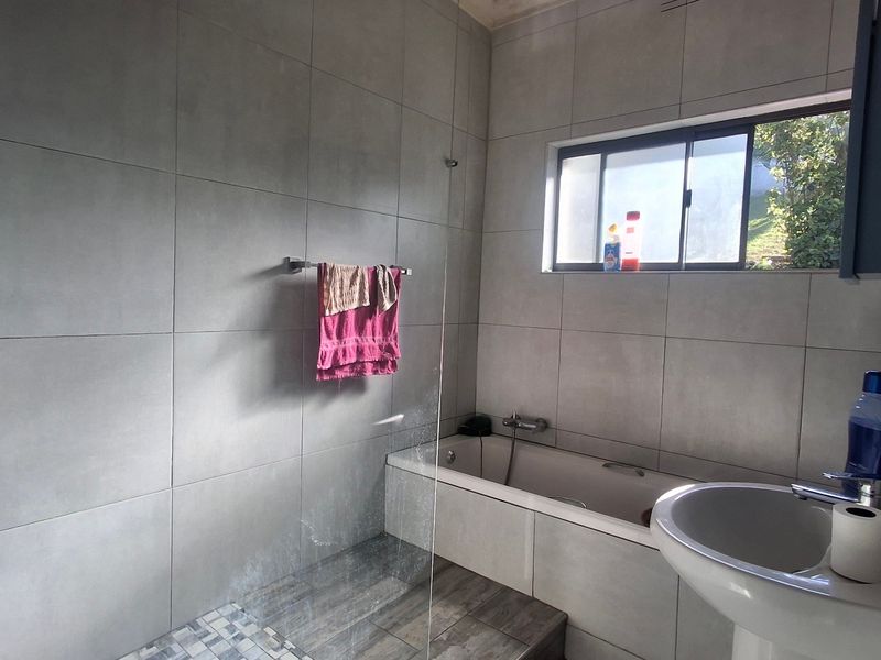 Modern bathroom featuring large format wall tiles, a built-in bathtub, a glass shower screen, and a pedestal basin with a sliding window.