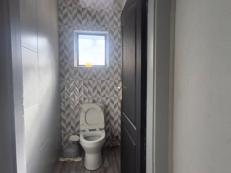 A compact guest bathroom featuring modern geometric patterned wall tiles, neutral floor tiling, and a standard toilet.