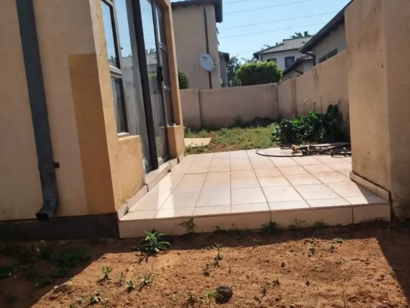 Rear exterior view of the apartment featuring a tiled patio area, sliding glass doors, and an unlandscaped garden space.