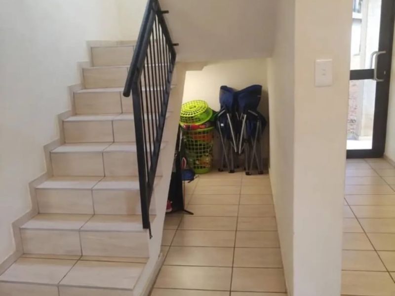 A bright hallway featuring tiled flooring and a staircase with a metal handrail, leading towards an exterior glass panel door.