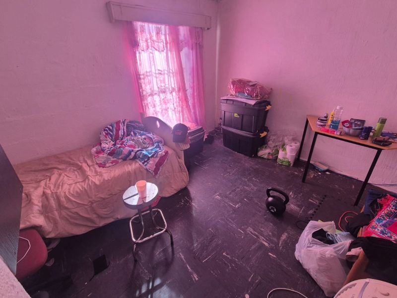 A bedroom featuring dark vinyl flooring and a window with a curtain rail, requiring cosmetic updates and maintenance to improve its overall condition.