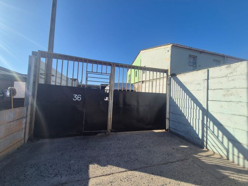 Front entrance view featuring a metal driveway gate and perimeter boundary wall with concrete driveway access.
