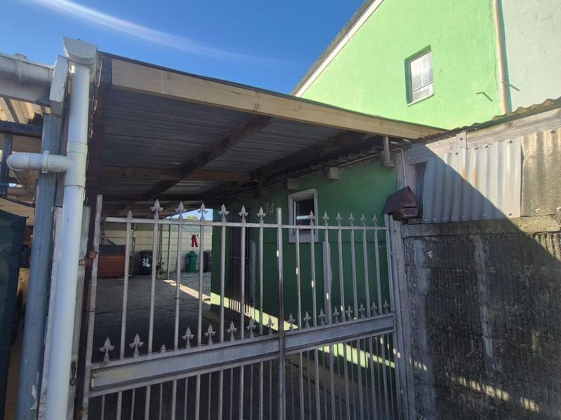 Front exterior view featuring a metal security gate, a basic carport structure, and a concrete driveway leading to the property entrance.