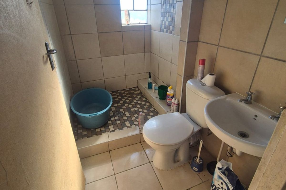 Compact bathroom featuring a shower area, pedestal basin, and toilet with neutral wall and floor tiling.