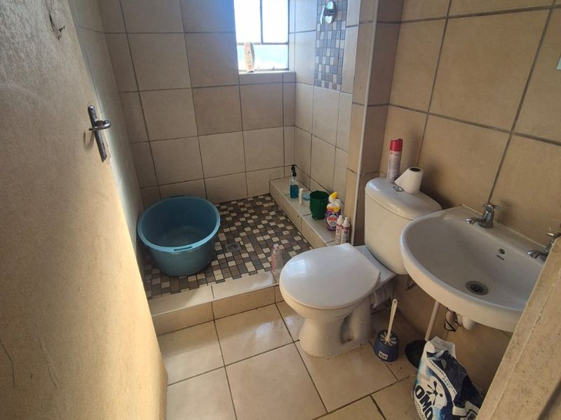 Compact bathroom featuring a shower area, pedestal basin, and toilet with neutral wall and floor tiling.