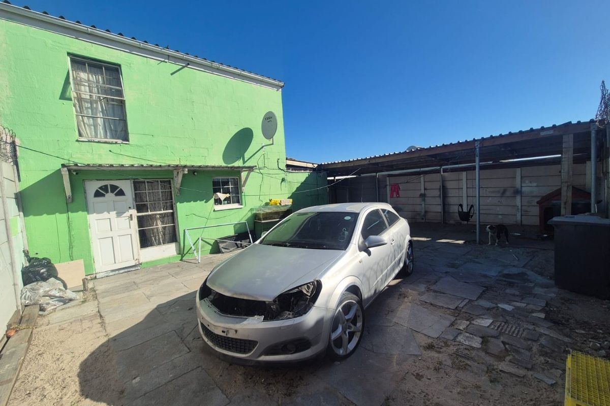 Rear exterior view of the property featuring a paved courtyard area and a covered carport structure.
