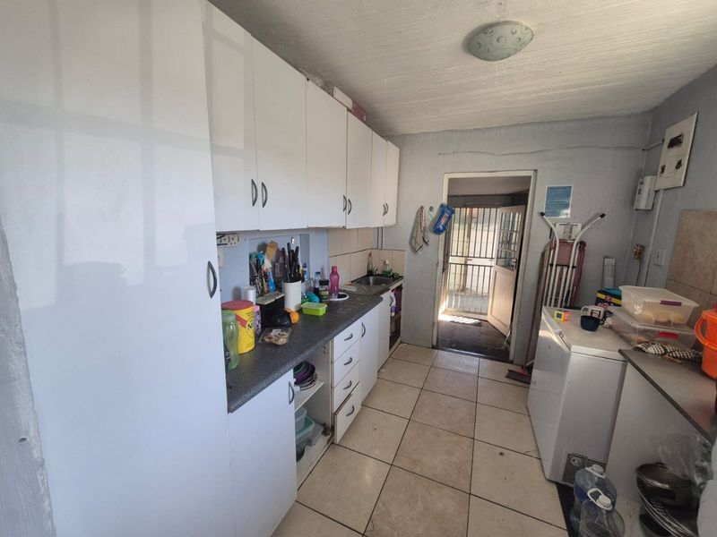 A functional scullery area featuring built-in white cabinetry, laminate countertops, a stainless steel sink, and tiled flooring with direct access to the exterior.