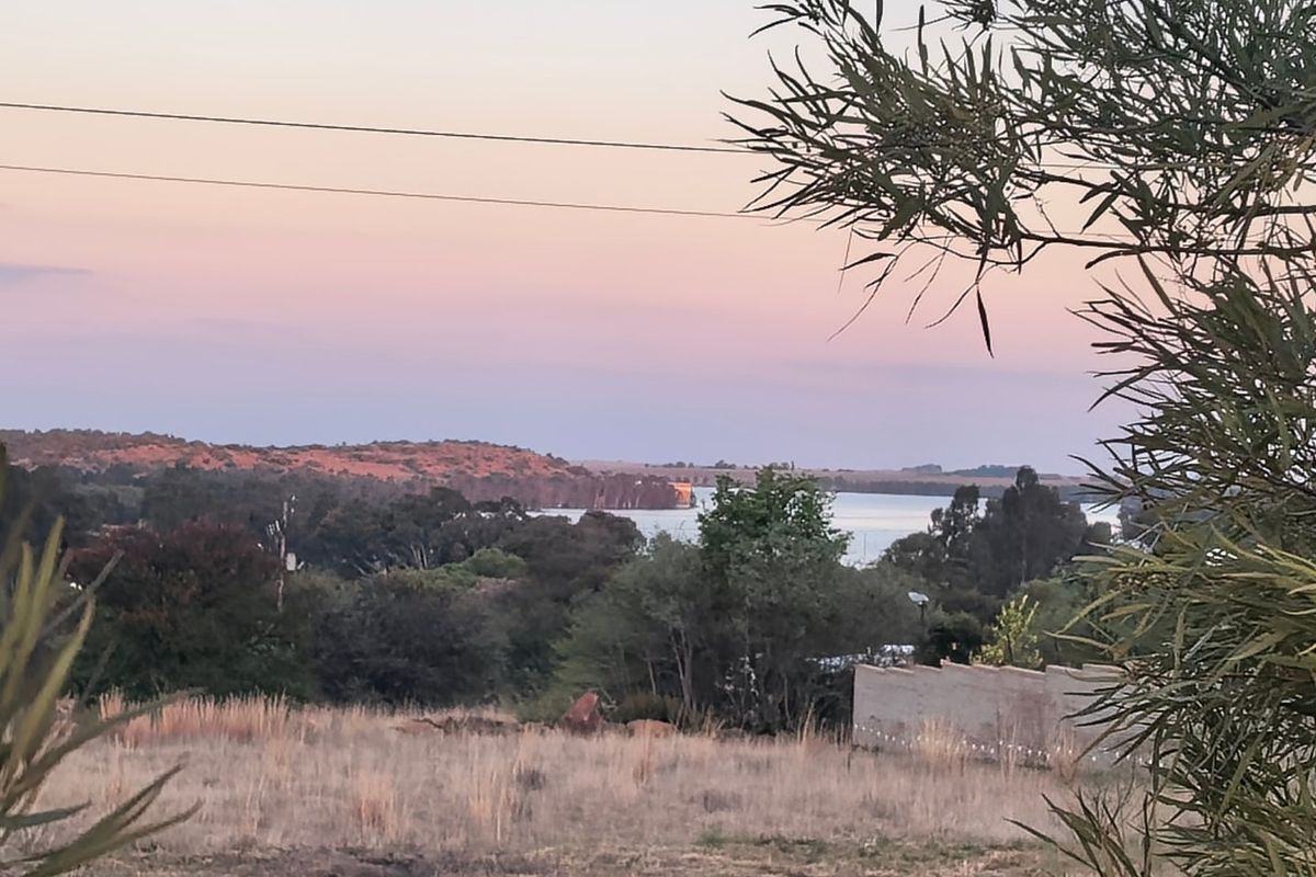 A scenic view overlooking a landscape with trees, distant hills, and a body of water at sunset.