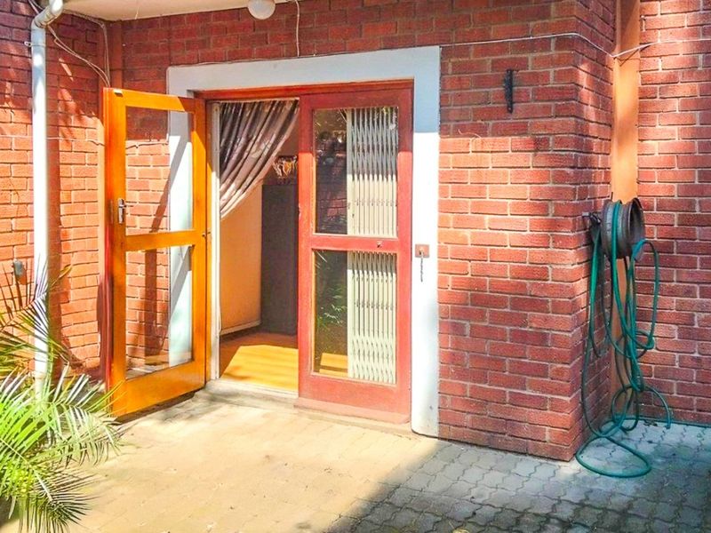 A paved patio area featuring a red brick exterior wall and a timber-framed door providing access to the interior living space.
