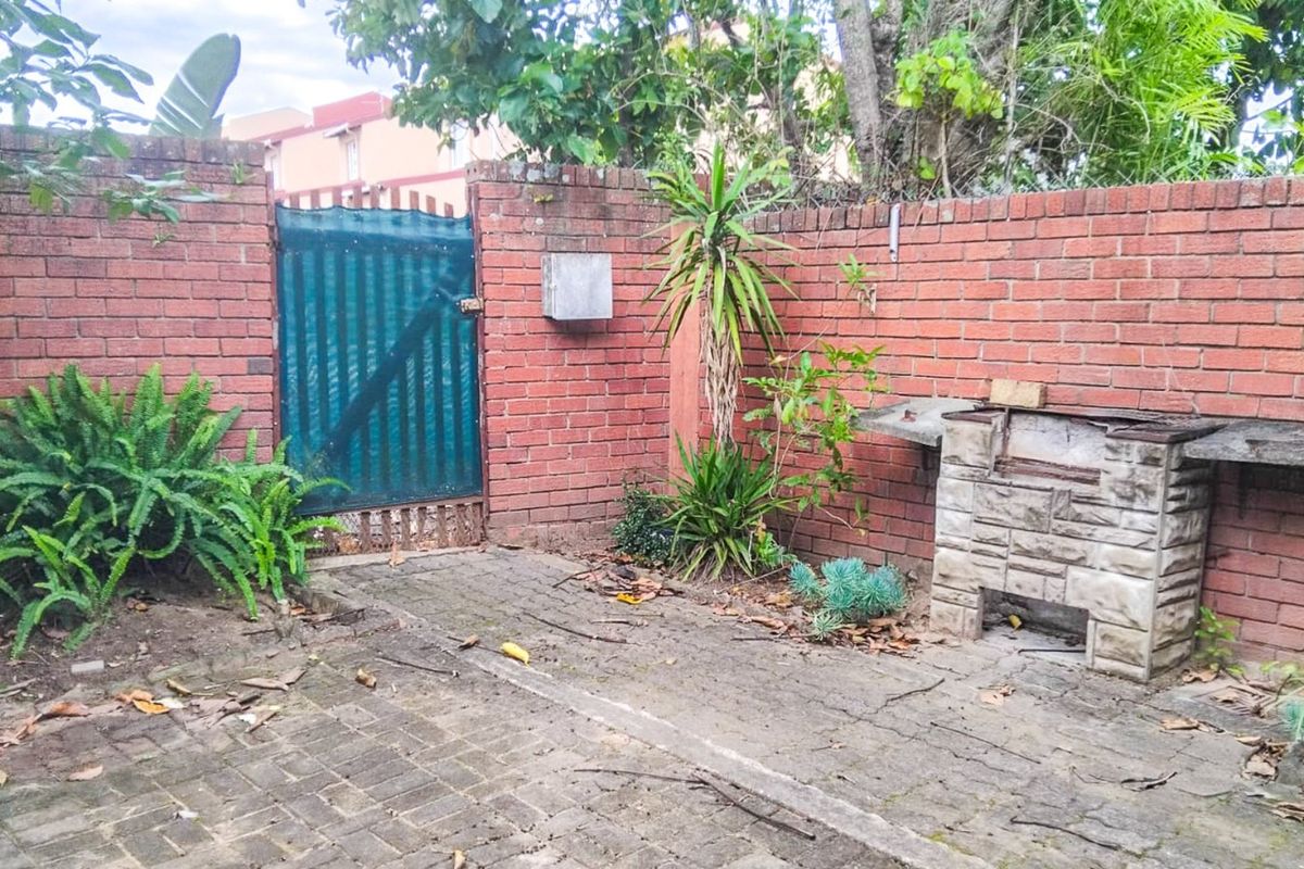 A private rear courtyard featuring a paved patio area, brick boundary walls, and a built-in braai, offering potential for outdoor entertainment space.