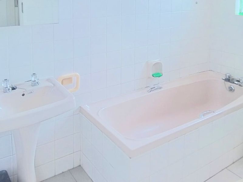 A functional bathroom featuring a pedestal basin and a built-in bathtub with classic white wall tiling.