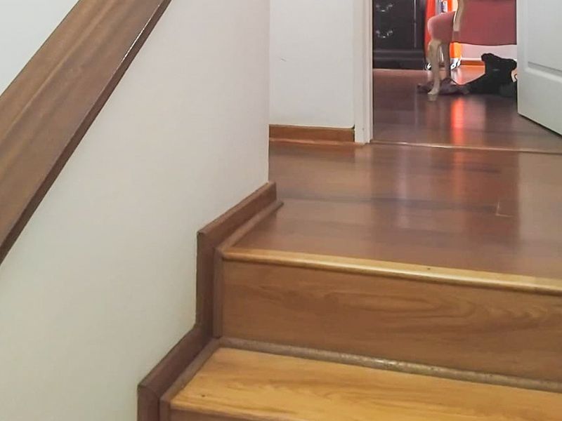 A view of a wooden staircase and hallway featuring laminate flooring and a wooden handrail.