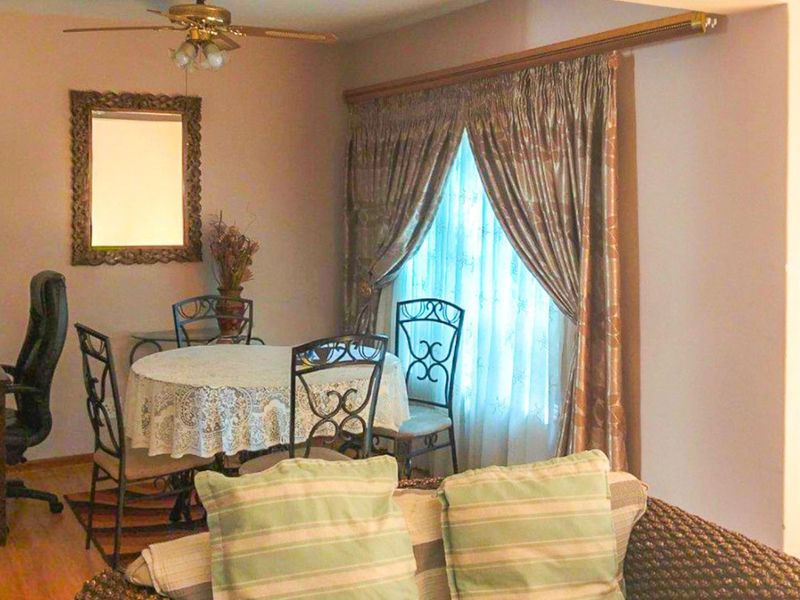 A living area featuring laminate flooring and a ceiling fan, with natural light entering through a window dressed with curtains.