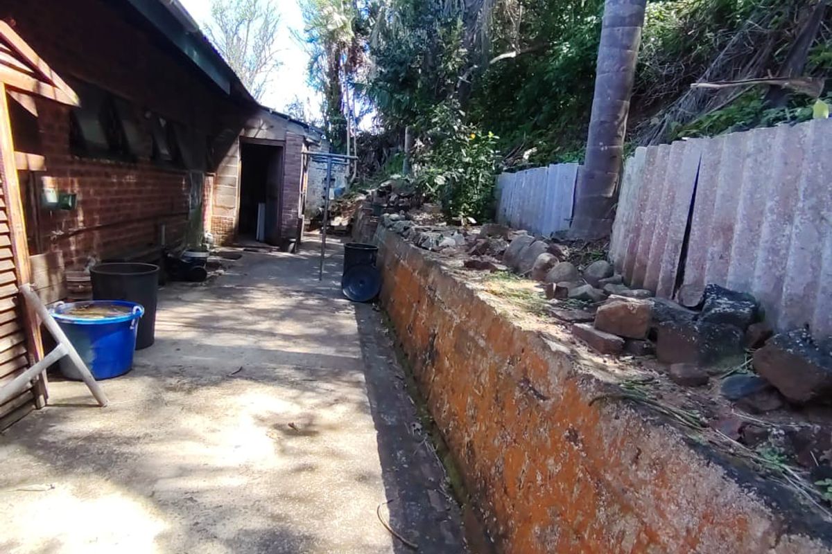 Rear exterior area featuring a concrete pathway, brick retaining wall, and mature trees along the boundary line.
