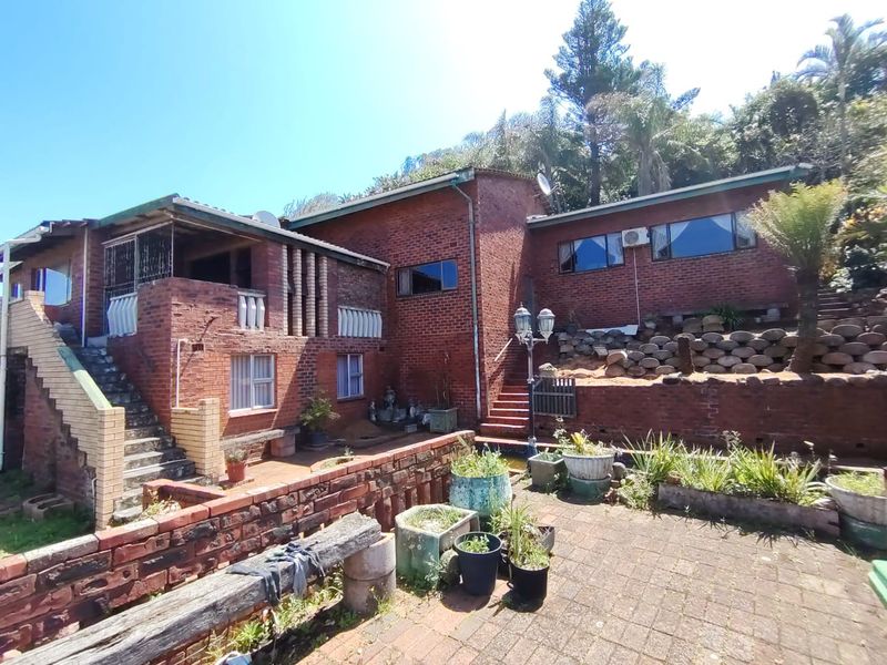 Rear view of a multi-level brick house featuring a paved patio area, retaining walls, and an external staircase leading to an upper balcony.