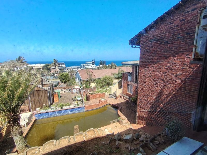 An elevated view of a backyard featuring a swimming pool with brick retaining walls and a view of the surrounding neighborhood and ocean.
