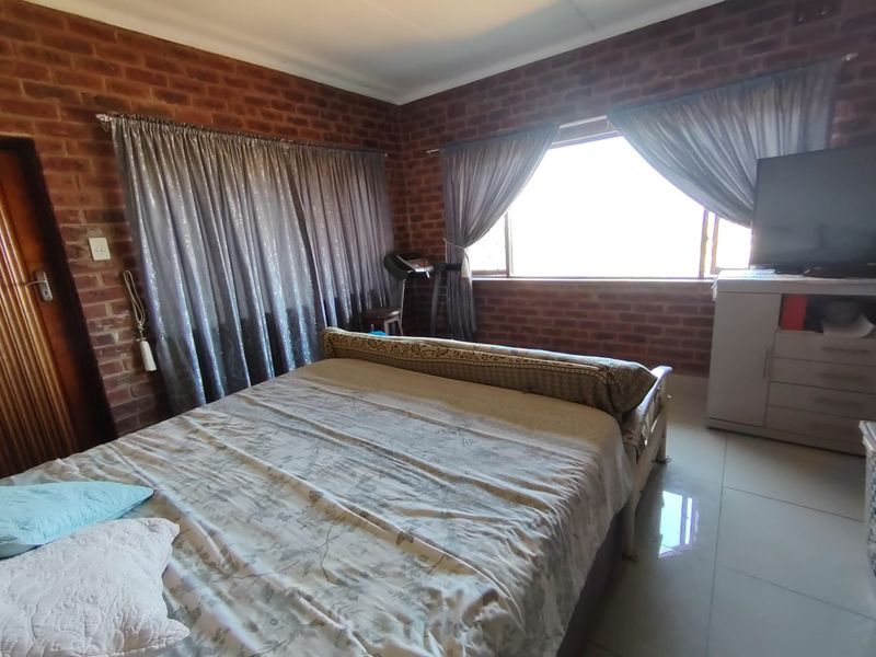 A bedroom featuring exposed brick walls, tiled flooring, and large windows that provide natural light.