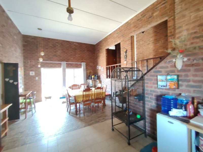 Spacious open-plan living and dining area featuring exposed brick walls, tiled flooring, and an internal staircase.