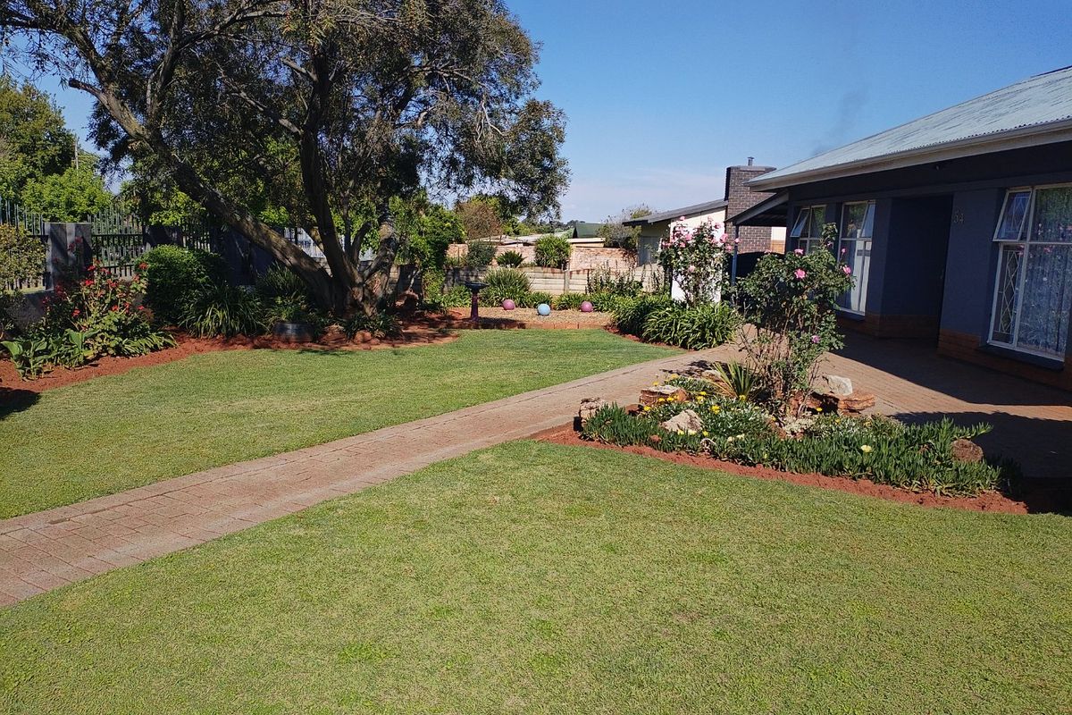 A well-maintained rear garden featuring a paved walkway, established trees, and landscaped flower beds adjacent to the house exterior.