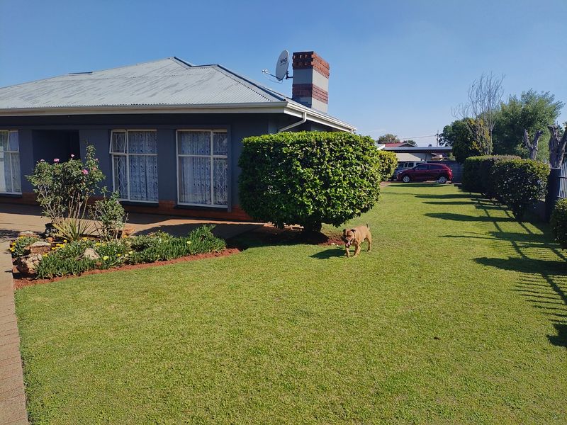 A well-maintained front exterior view of the house featuring a neat lawn, landscaped garden beds, and a paved walkway leading to the entrance.