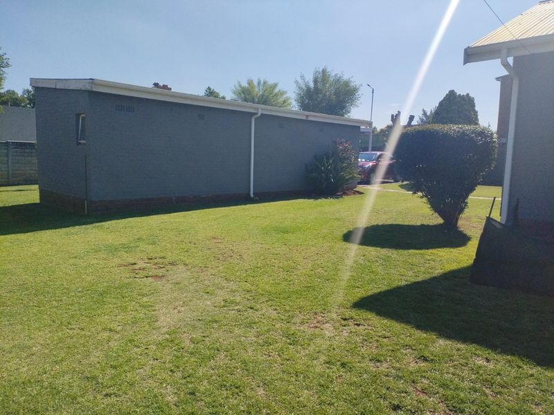 A view of the rear garden area featuring a lawn and the side elevation of an outbuilding with gutters and downpipes.