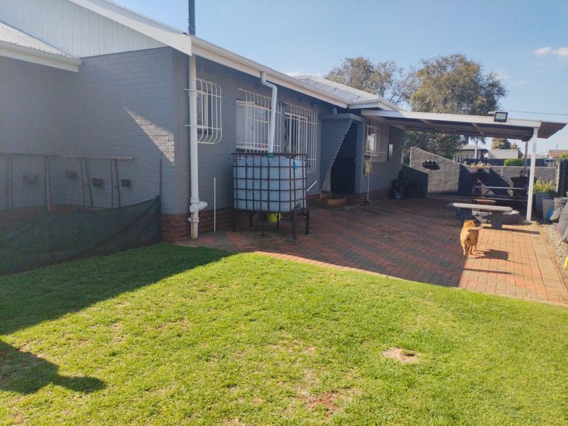 Rear exterior view featuring a paved patio area, covered outdoor space, and a well-maintained lawn with integrated rainwater storage.