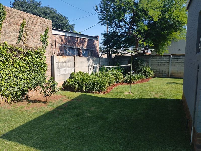 A private rear garden featuring a well-maintained lawn, established garden beds, and secure perimeter walling with a functional rotary clothesline.
