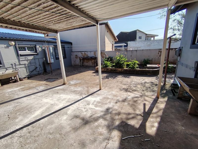 A spacious covered concrete patio area featuring a raised garden bed, external wash basins, and wall-mounted laundry facilities, requiring some maintenance and cosmetic updates.