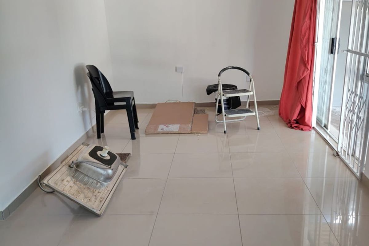 A bright, empty living room featuring neutral tiled flooring and a sliding glass door with security gate access to the exterior.