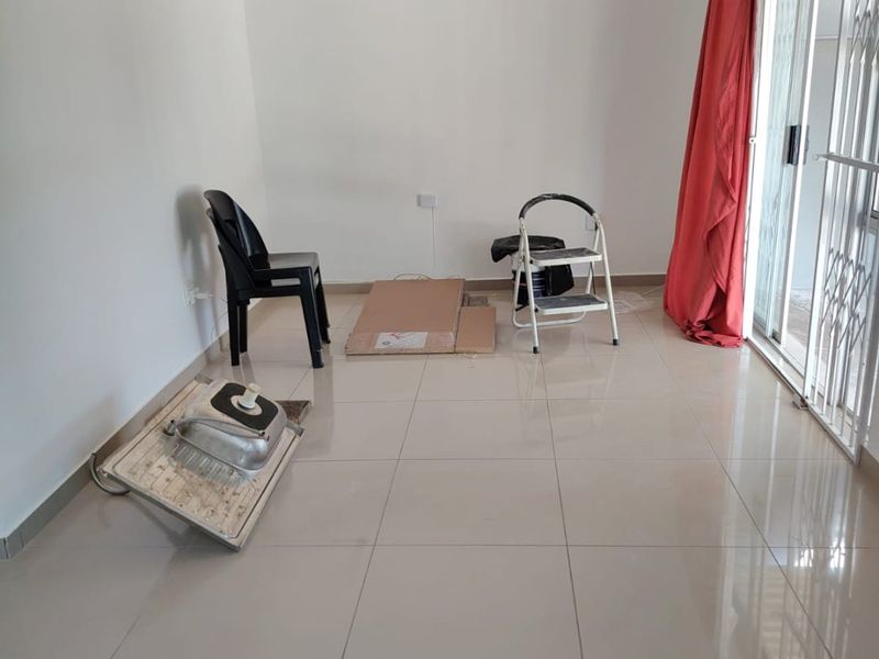 A bright, empty living room featuring neutral tiled flooring and a sliding glass door with security gate access to the exterior.