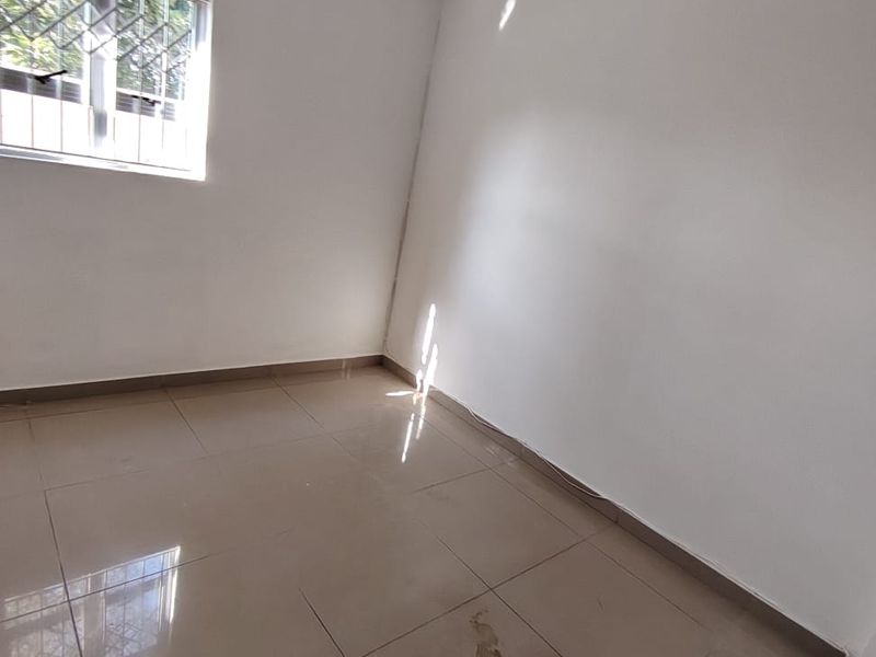 A vacant bedroom featuring neutral tiled flooring and a window fitted with security bars, offering a clean, blank canvas for personalization.