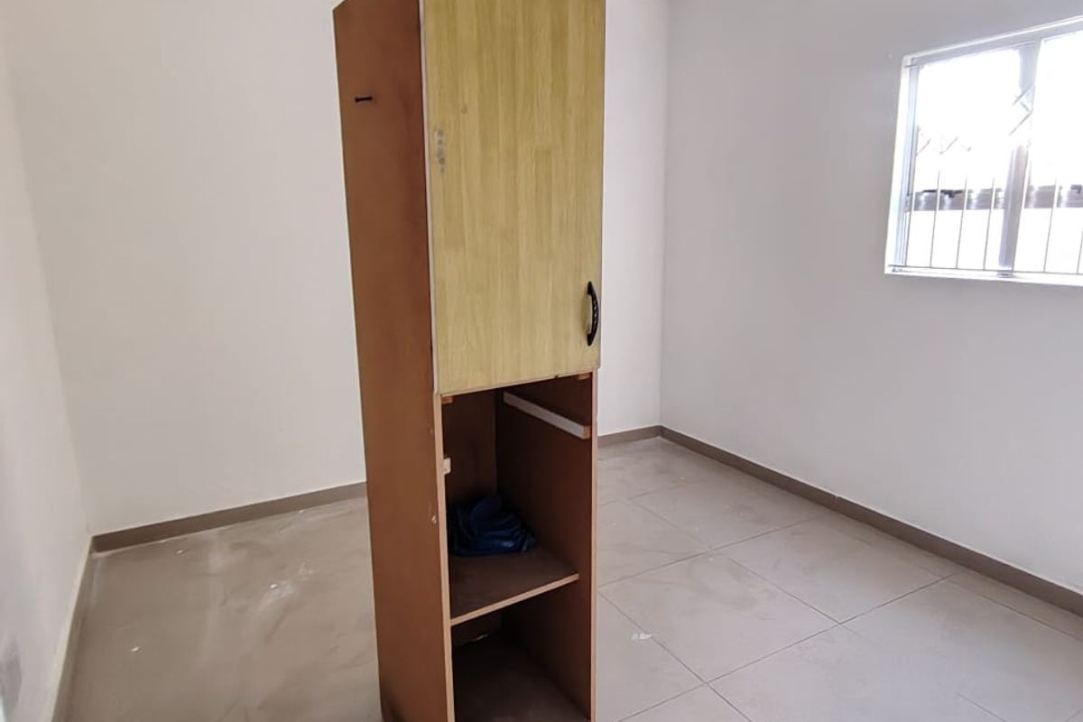 A vacant bedroom featuring tiled flooring and a window with security bars. The room includes a standalone storage unit requiring repair or removal.