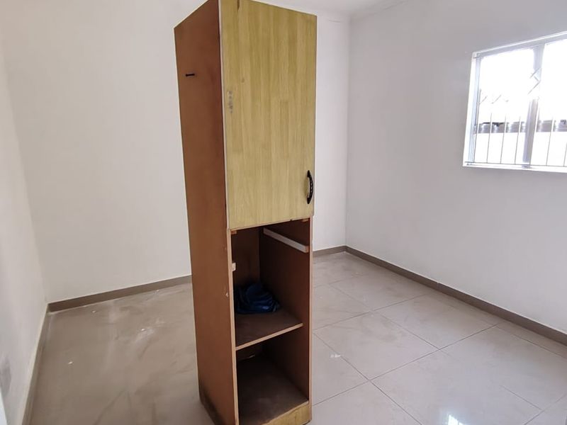A vacant bedroom featuring tiled flooring and a window with security bars. The room includes a standalone storage unit requiring repair or removal.