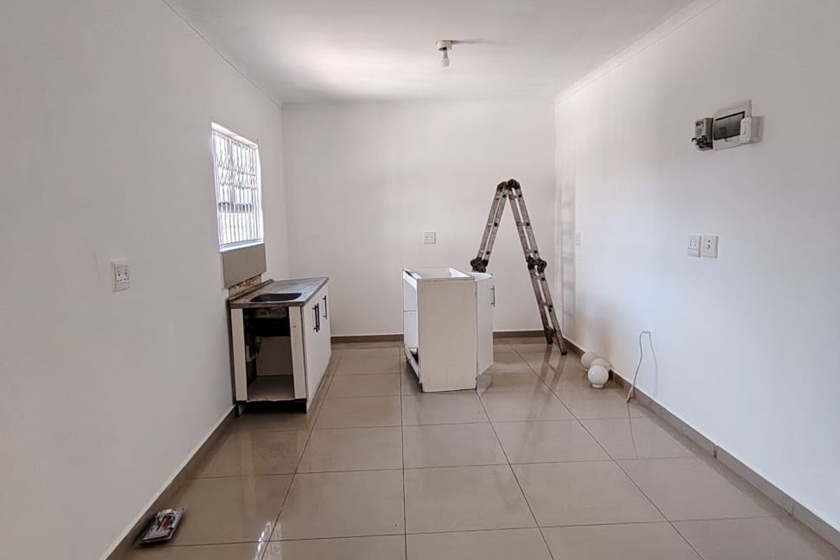 An empty, unfinished kitchen space featuring tiled flooring, a basic sink unit, and exposed electrical points, ready for final cabinetry and appliance installation.
