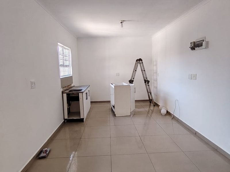An empty, unfinished kitchen space featuring tiled flooring, a basic sink unit, and exposed electrical points, ready for final cabinetry and appliance installation.