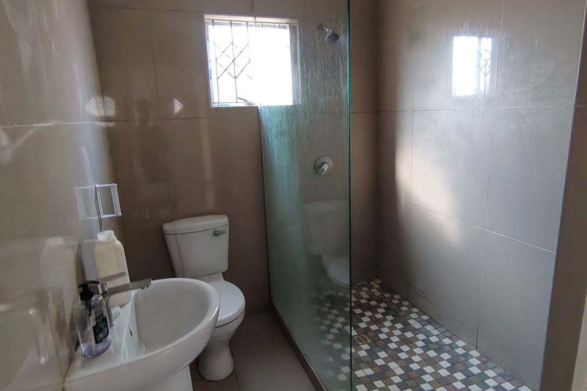 A functional bathroom featuring a pedestal basin, toilet, and a walk-in shower with a glass screen and mosaic floor tiling.