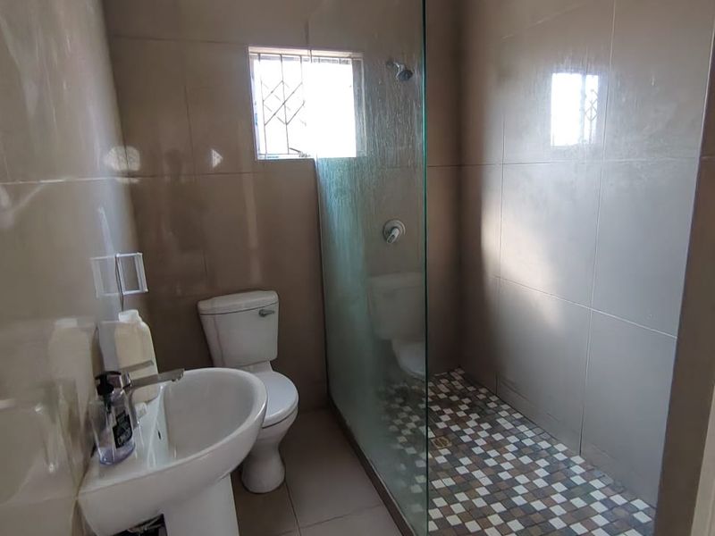 A functional bathroom featuring a pedestal basin, toilet, and a walk-in shower with a glass screen and mosaic floor tiling.