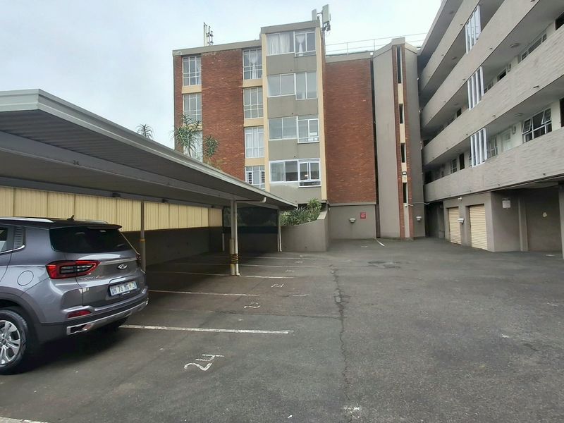An outdoor parking area featuring a covered carport structure and asphalt paving adjacent to the apartment building complex.