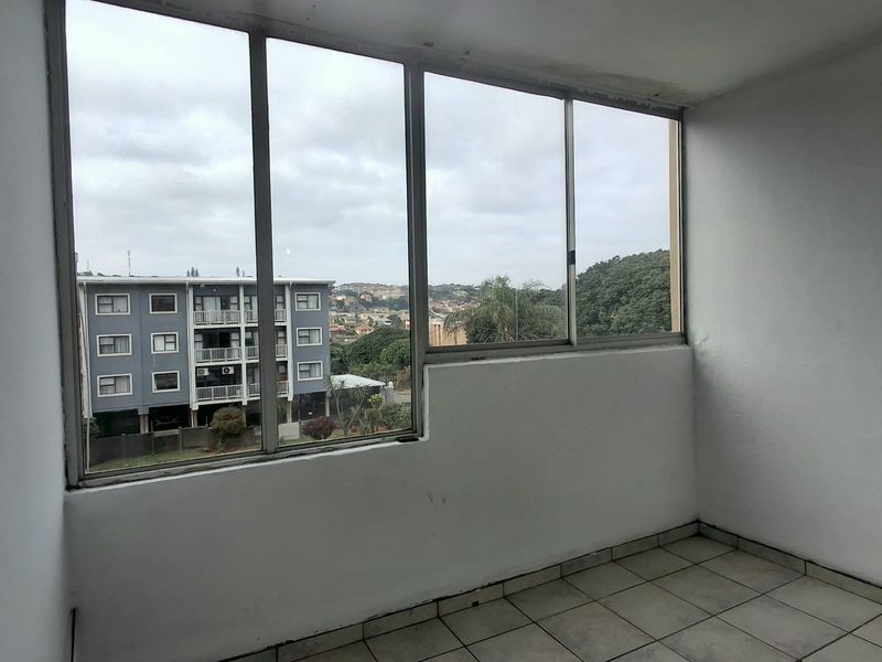 An enclosed balcony area featuring tiled flooring and large windows offering an elevated view of the surrounding neighborhood.