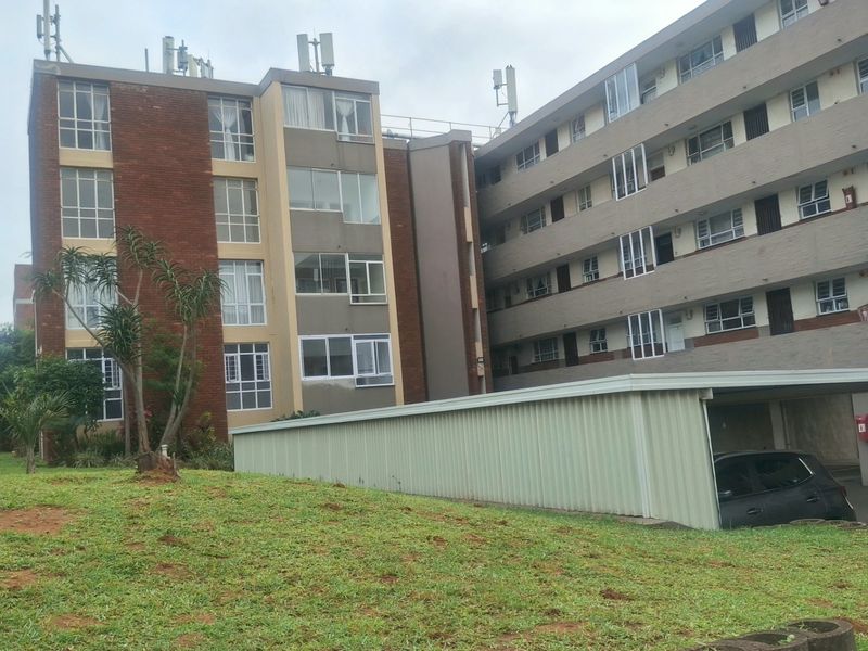 Exterior view of a multi-story apartment complex featuring brick and painted facades, aluminum windows, and a covered carport area.