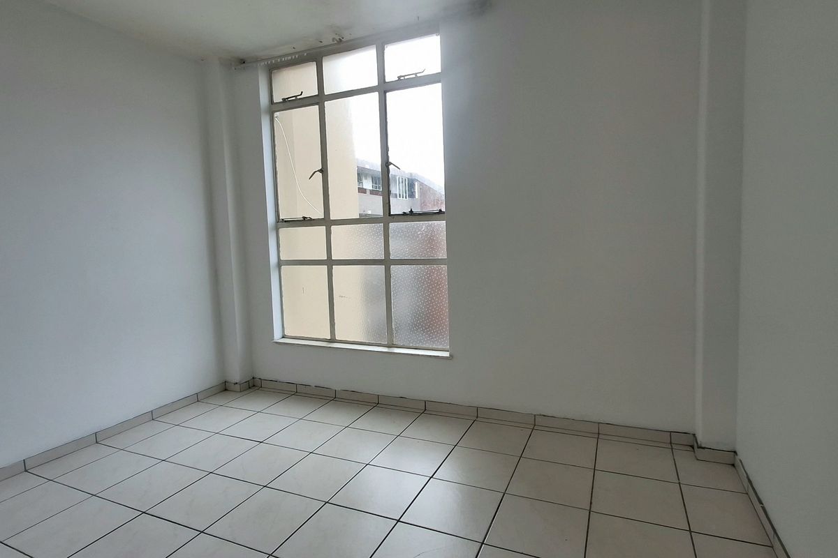 An empty bedroom featuring tiled flooring and a large multi-pane window, providing a blank canvas for potential interior design updates.