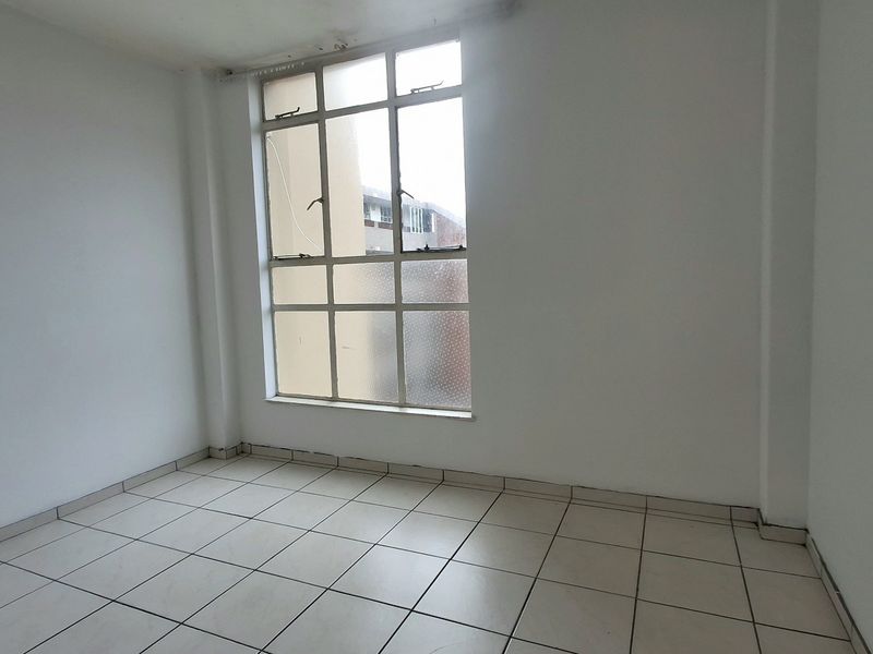 An empty bedroom featuring tiled flooring and a large multi-pane window, providing a blank canvas for potential interior design updates.