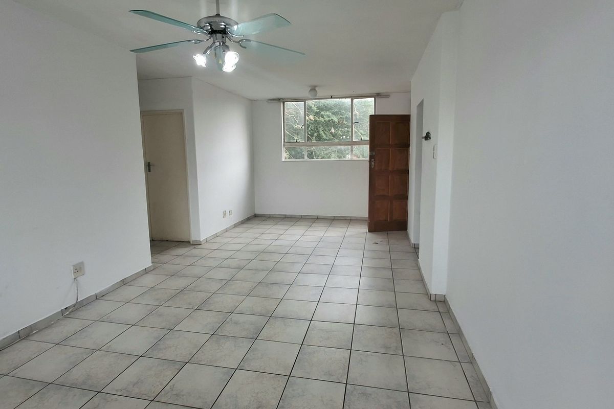 An empty, open-plan living area featuring neutral white walls, tiled flooring, and a ceiling fan, offering a blank canvas for interior design.